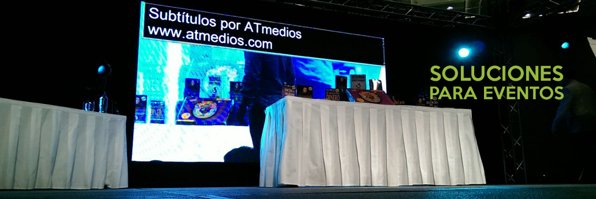 En la pantalla de un escenario el texto “subtítulos por ATmedios.